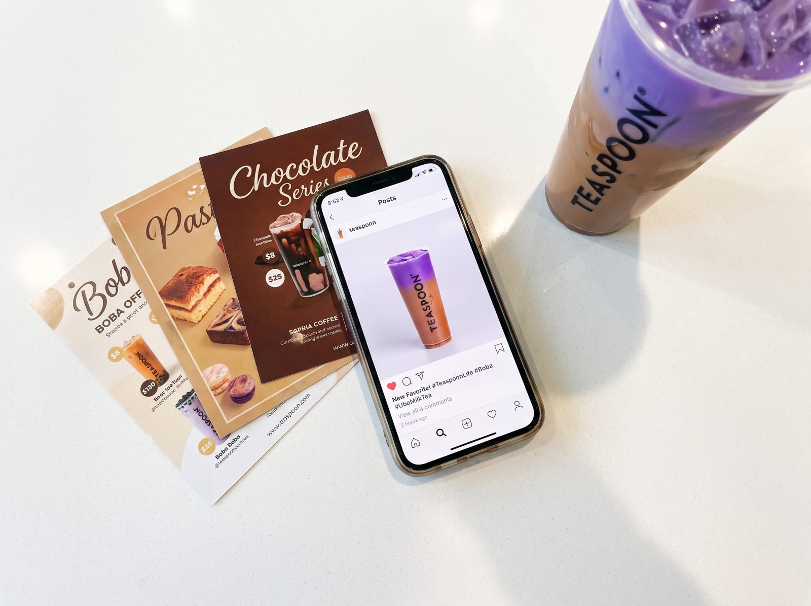 Teaspoon menu flyers and a phone showing the Instagram feed beside a taro drink.