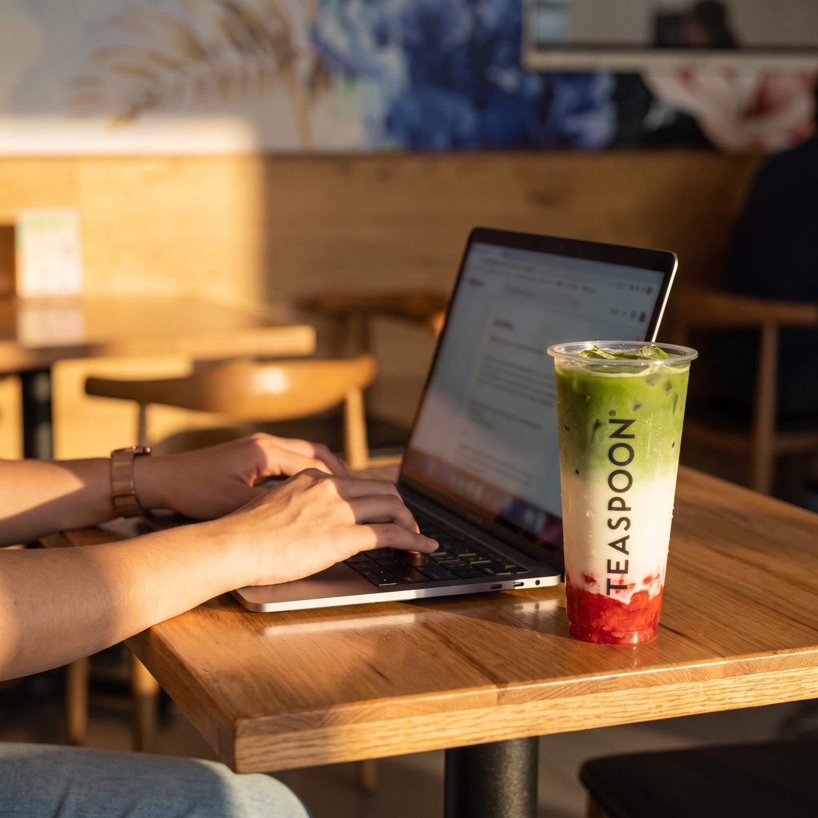 Someone filling out the franchise form on a laptop at a Teaspoon table, a matcha strawberry latte beside them.